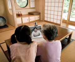 Two people looking at webcam video of a man through a notebook at home